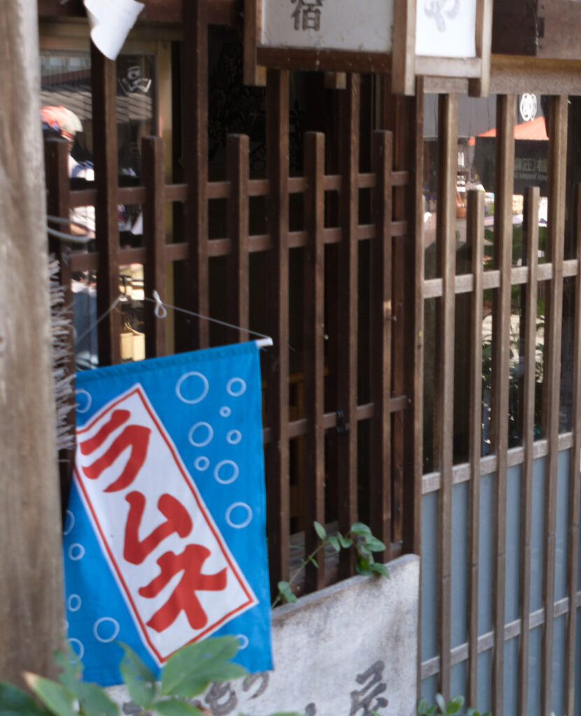 A ramune flag hanging by a traditional wooden lattice doorway evokes the atmosphere of summer in old Japan. Loved at festivals and neighborhood shops, ramune became a refreshing symbol of Japanese summer.